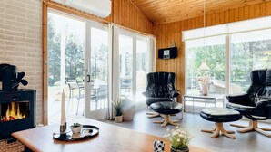 A cozy room with a fireplace, leather chairs, a wooden table, and large windows offering a view of the outdoors. - 6 Person Holiday Home in Strandby (Strandby)