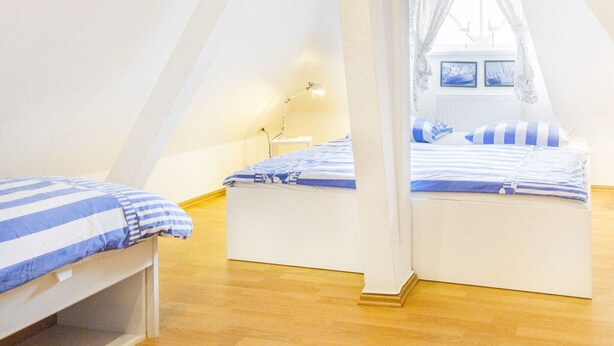 A cozy attic bedroom with two beds, wooden flooring, and a window with a view of the outside. - Landhaus Wildrose Comfortable Holiday Residence (Binz)
