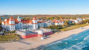 A coastal hotel with a large building featuring multiple red-roofed towers, a beach, and a view of the sea. - Landhaus Wildrose Comfortable Holiday Residence (Binz)