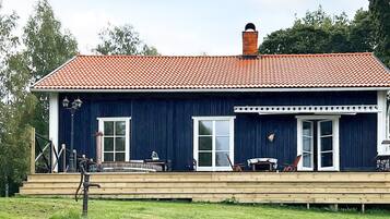 A two-story building with a red-tiled roof, a wooden deck, and a large window.