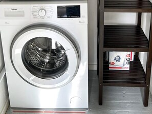 A front-loading washing machine with a control panel, a wooden shelf unit, and a box underneath. - 4 Star Holiday Home in Tronodal (Trönödal)