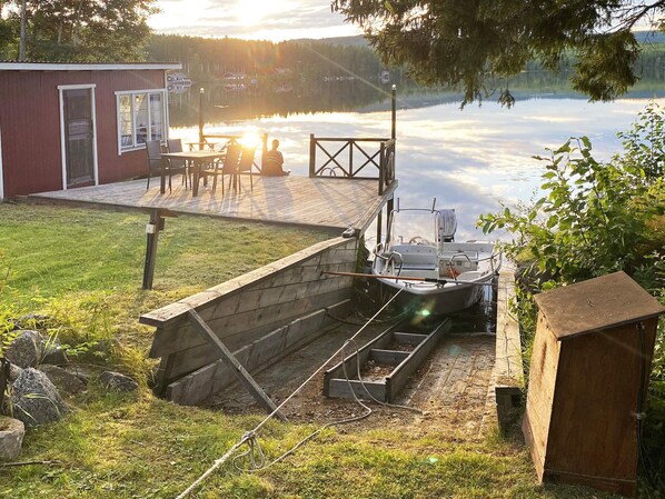A dock with a boat, a small shed, and a building with a deck overlooking a lake. - 4 Star Holiday Home in Tronodal (Trönödal)