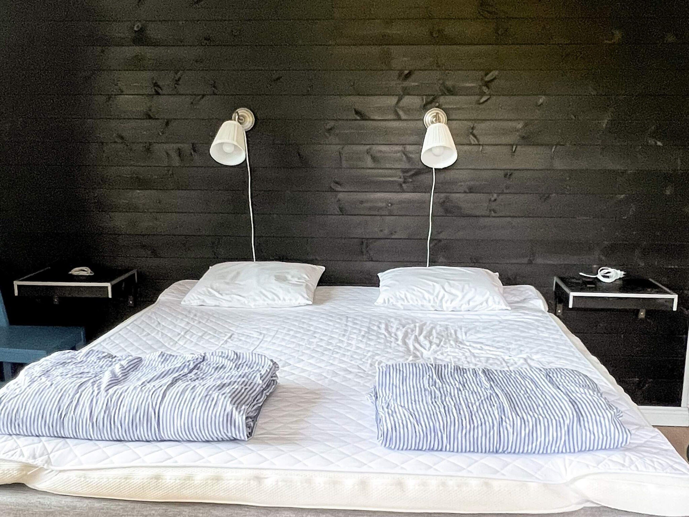 Una cama con dos almohadas, una mesita de noche y una lámpara a cada lado.