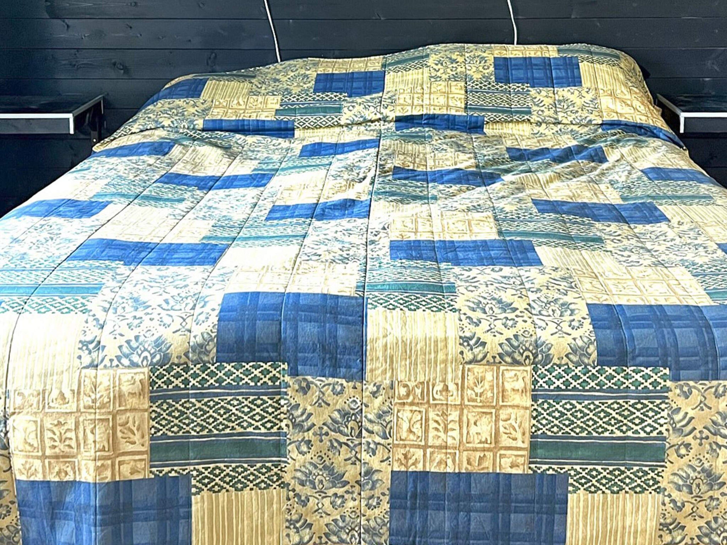 A bed with a quilted bedspread featuring geometric and floral patterns.