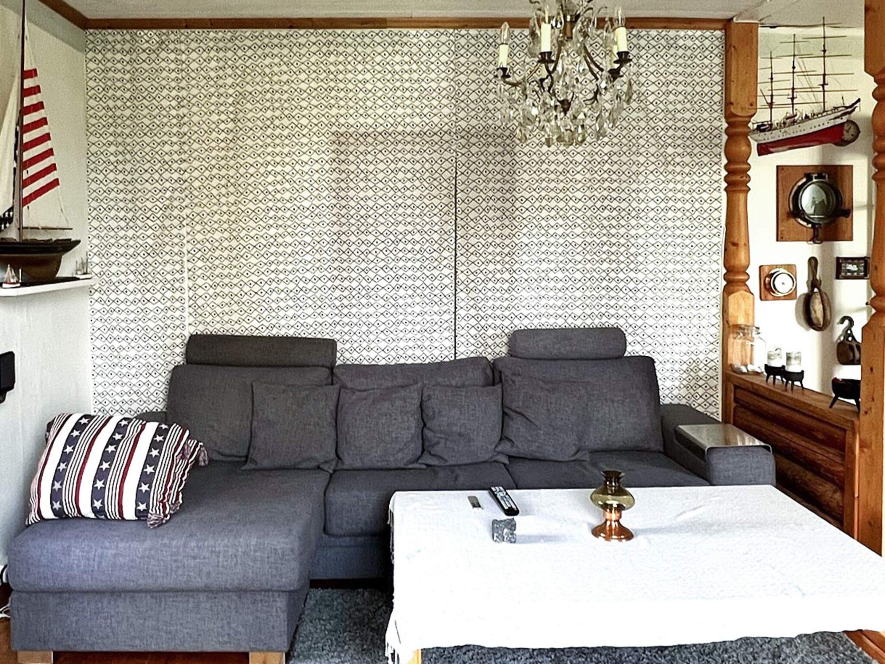 A modern living room with a sectional sofa, a chandelier, and a patterned wallpaper.