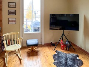 A room with a wooden floor, a rocking chair, a television on a tripod stand, and a window with a view of the outside. - 4 Star Holiday Home in Tronodal (Trönödal)