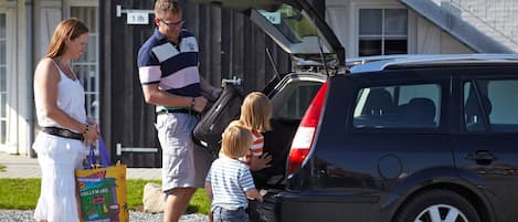 A family with a child opening a car trunk, standing in front of a building with a staircase.