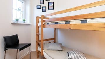 A bunk bed with a ladder, a desk, and a chair in a room with a window and wall-mounted pictures.