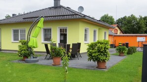 A yellow house with a tiled roof, a satellite dish, and a patio with chairs and potted plants. - Holiday Home Sonnentau (Burg (Spreewald))