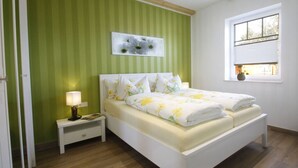 A bedroom with a bed, a nightstand, a lamp, a window, and a green-striped wall. - Holiday Home Sonnentau (Burg (Spreewald))