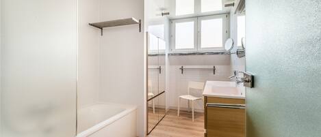 A modern bathroom with a glass shower enclosure, a wooden vanity, and a white chair.
