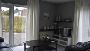 A modern living room with a sofa, a coffee table, and a TV. There is a sliding glass door leading to an outdoor area. - Holiday Apartment Mosselbank 95 (Ouddorp)