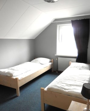 Een kleine kamer met twee eenpersoonsbedden, een raam met gordijnen en een radiator.