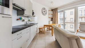 A modern kitchen with white cabinets, a black countertop, and a dining area with a wooden table and chairs. - Fiesole 201 Very Centrally Located in Koksijde (Koksijde)