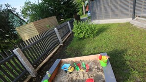 A sandbox with toys and a bucket, surrounded by a wooden fence and grass. - Gutsweg One - Apartment 3 (Eibenstock)