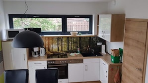 A compact kitchen with a dining area, a microwave, a kettle, and a window with a view of trees. - Gutsweg One - Apartment 3 (Eibenstock)