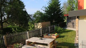 A backyard with a wooden table and benches, surrounded by potted plants and a wooden fence. - Gutsweg One - Apartment 3 (Eibenstock)