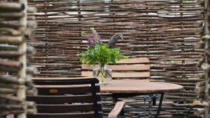 A rustic outdoor seating area with a round table and wooden chairs, surrounded by a woven fence. - Holiday Apartment Domstag (Kronsgaard)