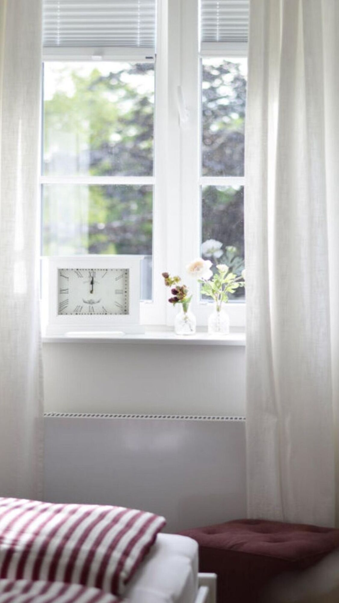 Une chambre avec une fenêtre, une horloge et deux vases de fleurs.