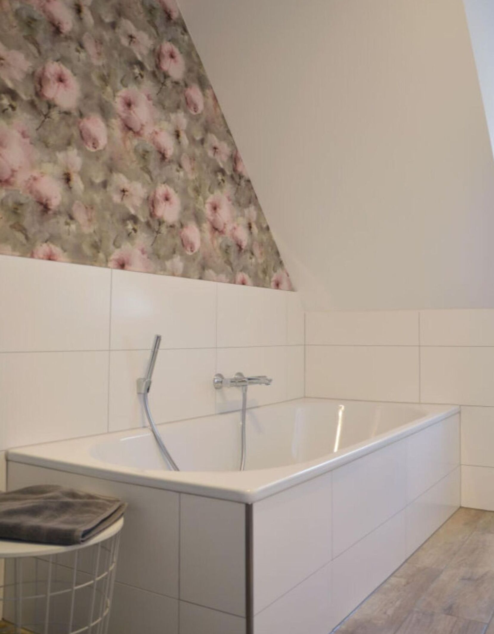Une salle de bain moderne avec une baignoire sur pieds, des carreaux blancs et un papier peint à motifs floraux qui apporte une touche d’originalité.