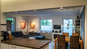 A modern kitchen with a dining area, featuring a kitchen island, built-in cabinets, and a seating area with a sofa and chairs. - Hexengluck Hahnenklee (Goslar)