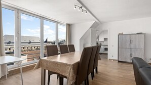 Un apartamento moderno con comedor, cocina y grandes ventanales que ofrecen vistas a la ciudad.