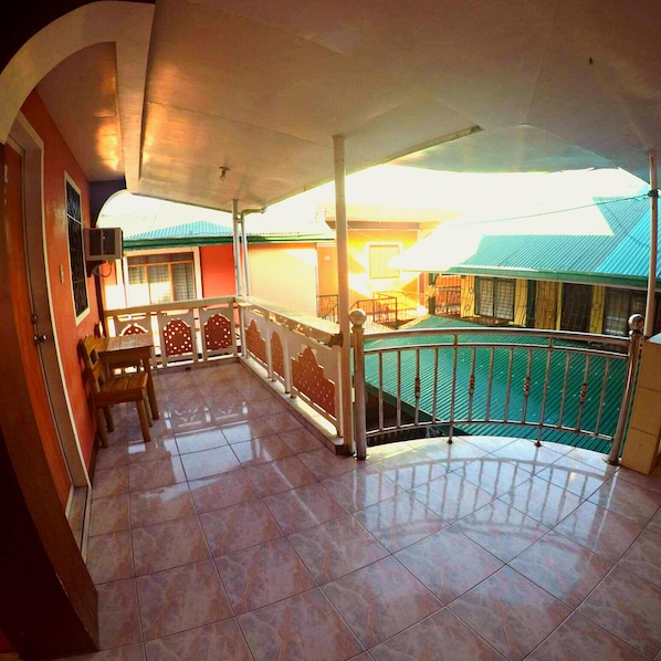 A covered balcony with tiled flooring, a wooden table with chairs, and a railing.
