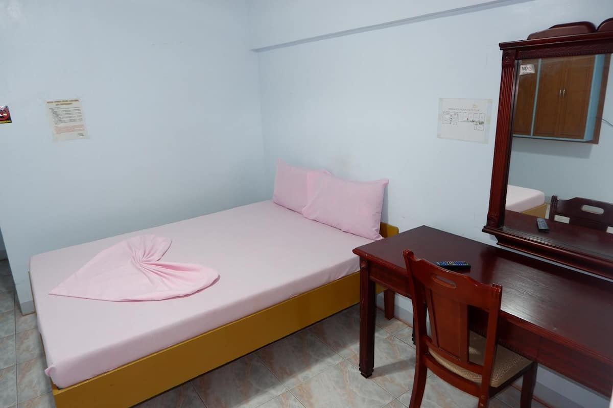 A small room with a single bed, a wooden desk, and a mirror.