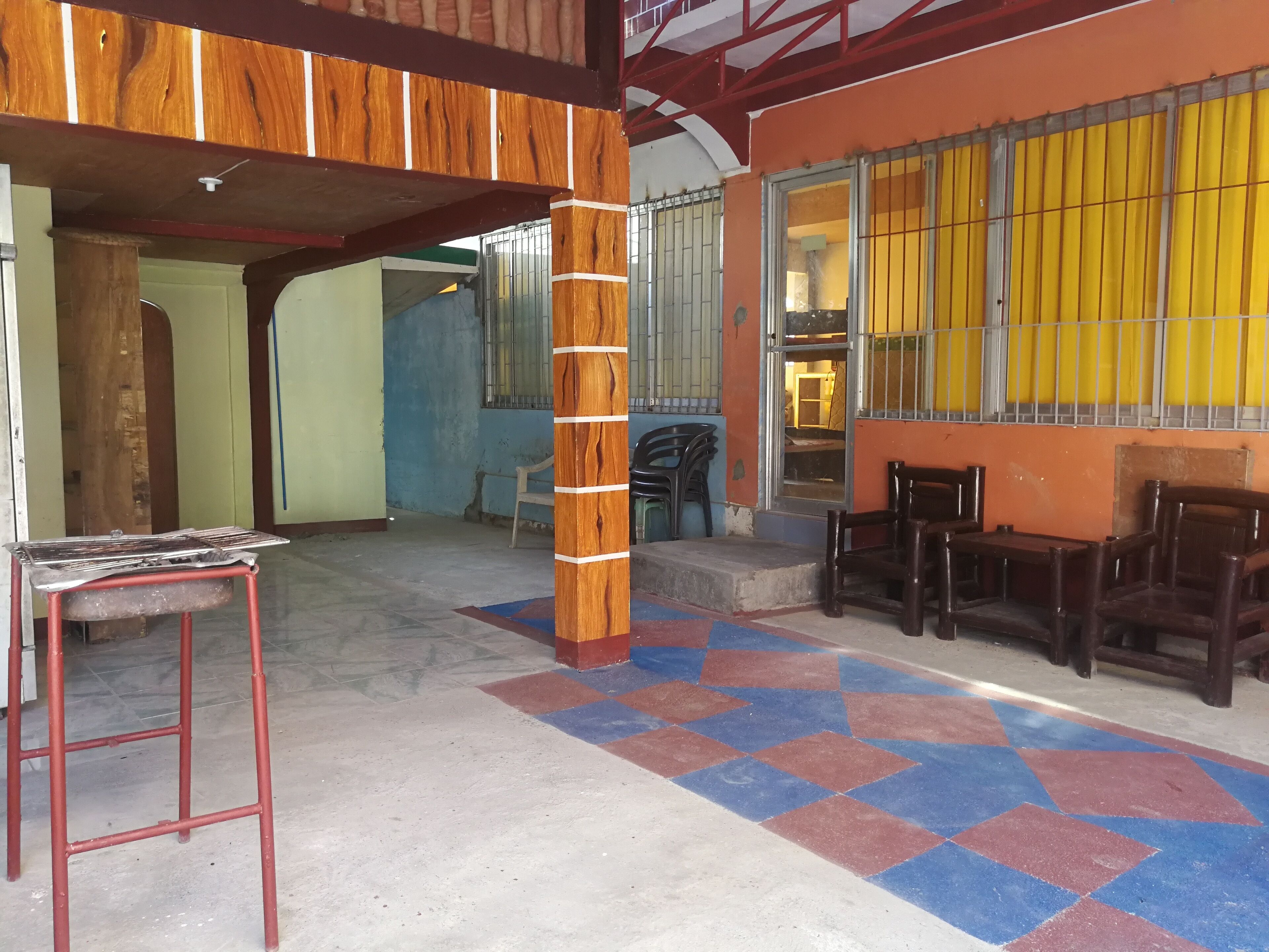 A spacious indoor area with a tiled floor, wooden furniture, and a large window with yellow blinds.