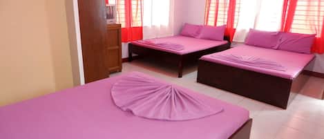 A hotel room with two beds, each with a purple bedspread and pillows. The room has red curtains and a wooden dresser.