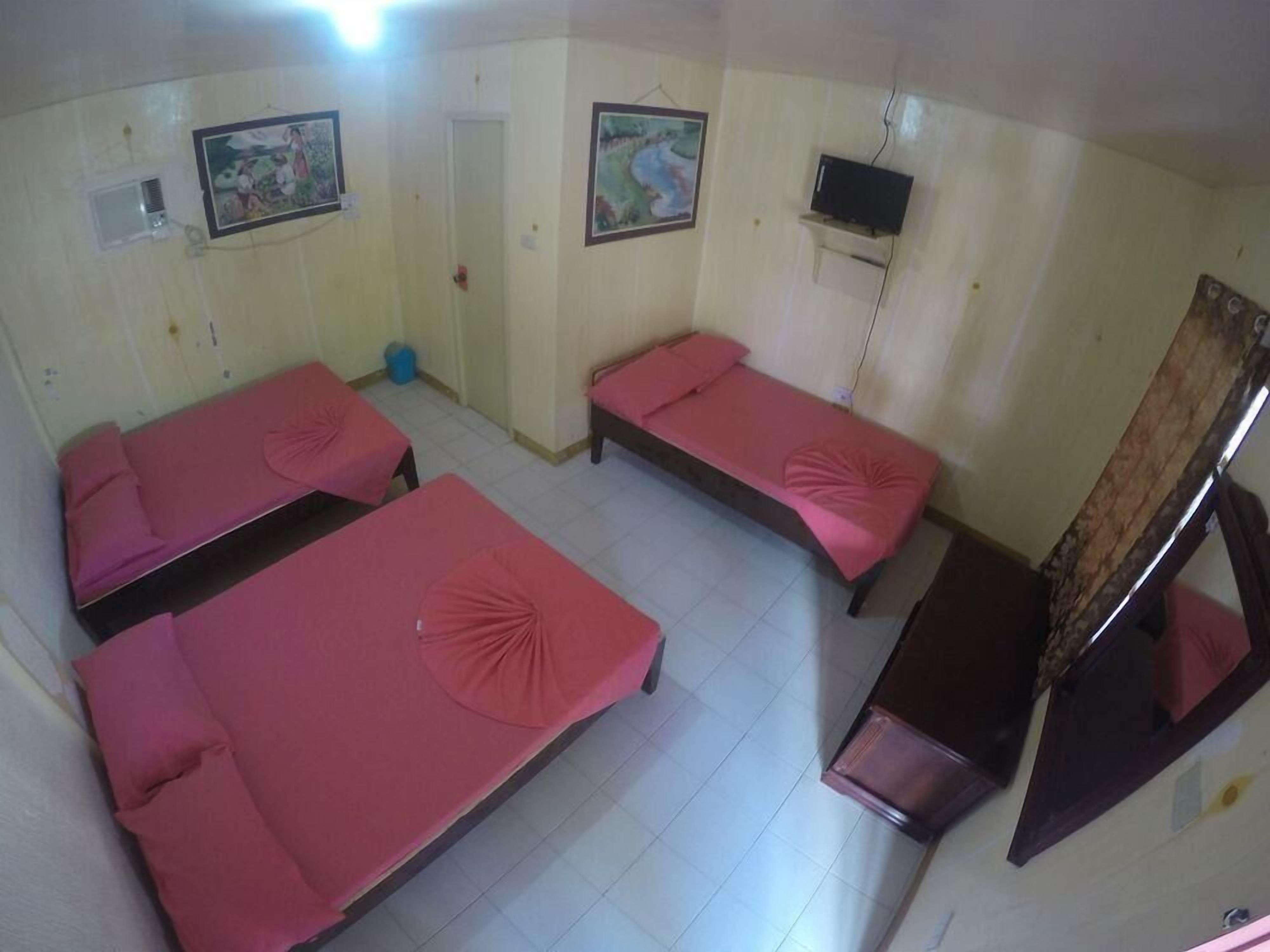 Una habitación con tres camas individuales, un televisor en la pared y una ventana pequeña.