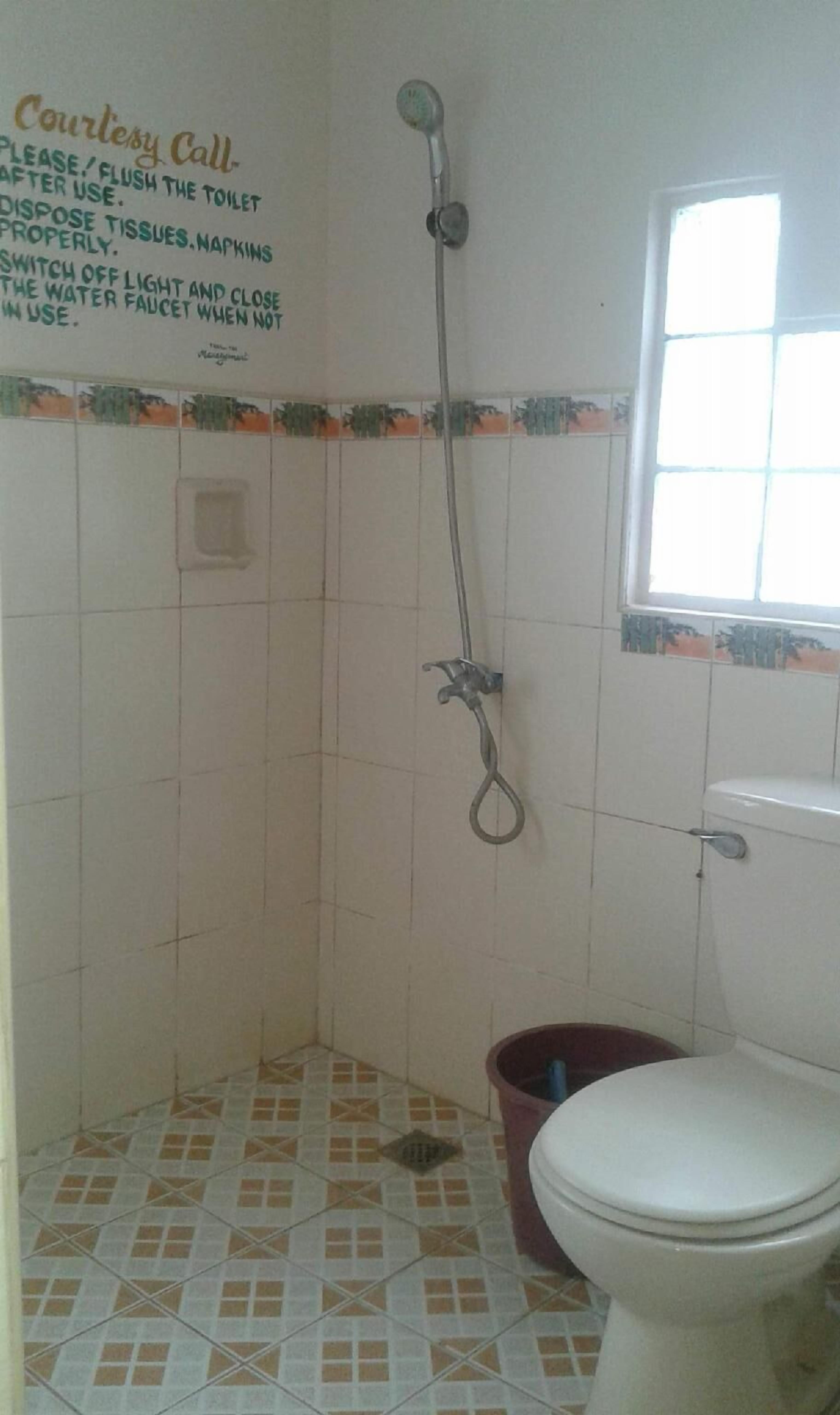 A small bathroom with a shower, toilet, and a window.