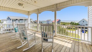 A wooden deck with rocking chairs and a view of houses and the ocean. - Gorgeous 2nd Row Home with Amazing Ocean Views, 2 Large Decks, Dog Friendly, Sleeps 12 (Oak Island)