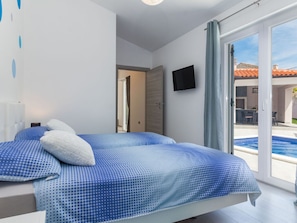 Een slaapkamer met twee bedden, een televisie en een schuifdeur naar een zwembad.