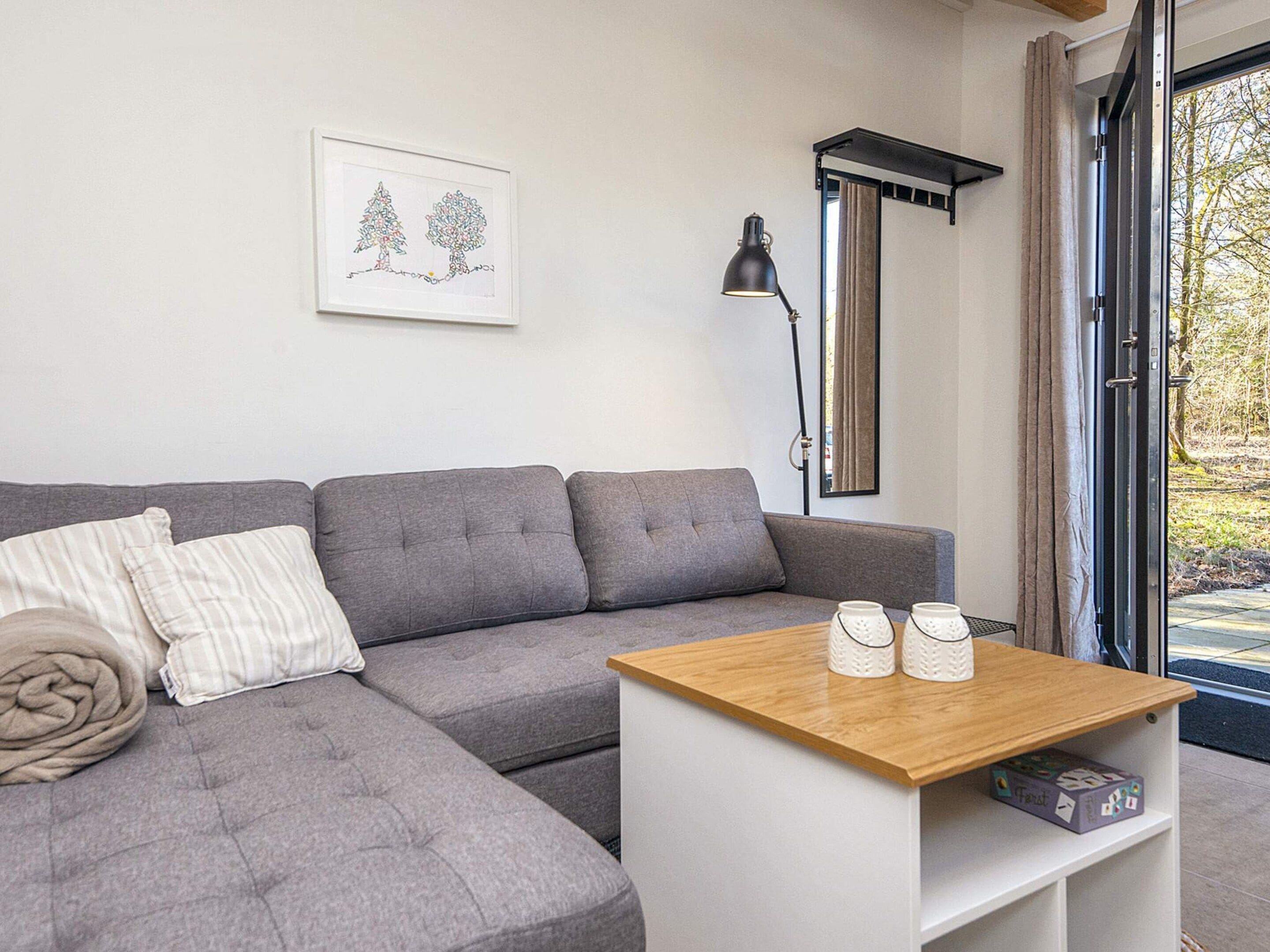 A modern living room with a grey sectional sofa, a wooden coffee table, and a framed artwork on the wall.