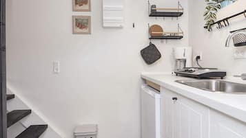 A modern kitchen with white cabinetry, a stainless steel sink, and a coffee maker.