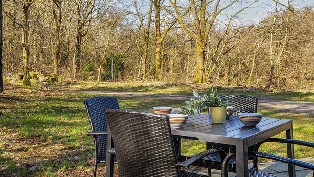 An outdoor dining area with wicker chairs and a table, surrounded by trees. - 5 Star Holiday Home in Hovborg (Hovborg)