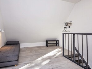 A loft bedroom with a grey sofa, a small table, and a staircase with a metal railing. - 5 Star Holiday Home in Hovborg (Hovborg)