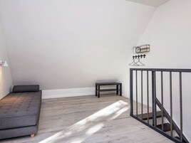 Un dormitorio tipo loft con un sofá gris, una mesita pequeña y una escalera con barandilla de metal.
