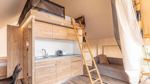 Une petite cuisine moderne et fonctionnelle, dotée d’une cuisinière intégrée, d’un évier et de placards de rangement. Une échelle en bois permet d’accéder à une zone de couchage située en mezzanine.