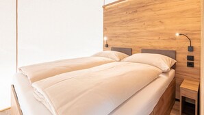 Un lit double avec une tête de lit en bois, des tables de chevet et des lampes fixées au mur.