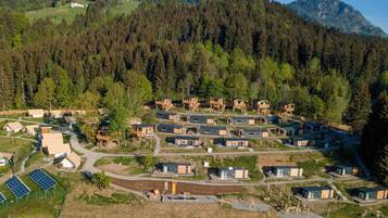 Una zona boscosa con varias cabañas de madera y algunos edificios más grandes, rodeada de colinas y una montaña al fondo.