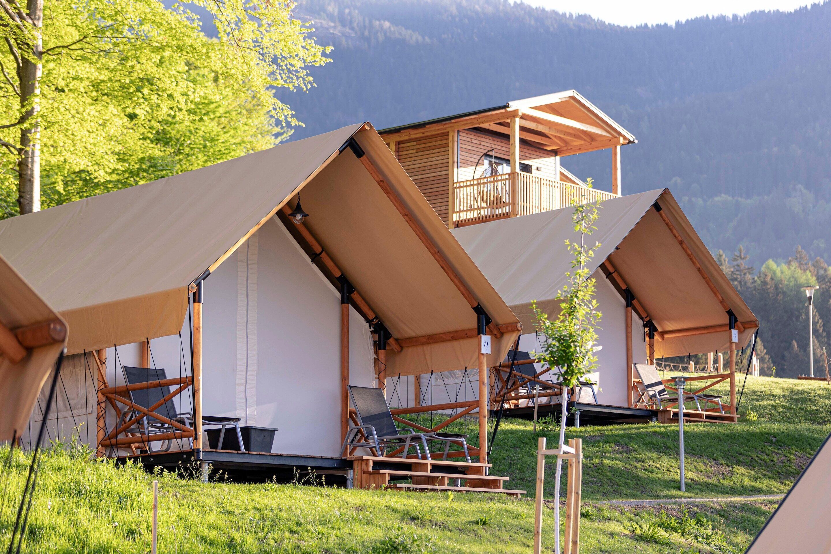A series of tents with wooden balconies and a grassy hillside backdrop.