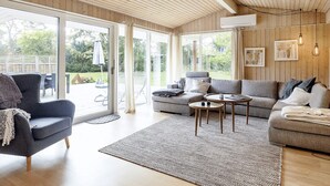 A spacious living room with a large sliding glass door leading to an outdoor area, a grey sofa, a dark armchair, and a coffee table. - 4 Star Holiday Home in Idestrup (Idestrup)