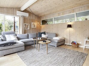 A modern living room with a sectional sofa, a round coffee table, and a large window providing a view of the outdoors. - 4 Star Holiday Home in Idestrup (Idestrup)