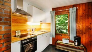 A kitchen with a brick wall, wooden cabinets, a stove, and a window with curtains. - Forest House in the Roman Valley (Morsbach)