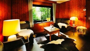 A cozy room with wooden walls, a leather sofa, a coffee table, and a cowhide rug. - Forest House in the Roman Valley (Morsbach)