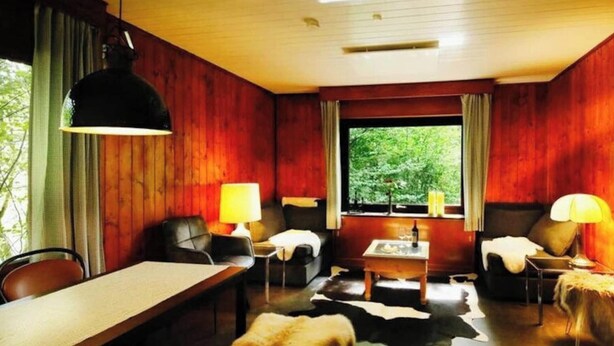 A cozy room with a wooden interior, a dining table, a sofa, and a window with a view of greenery. - Forest House in the Roman Valley (Morsbach)