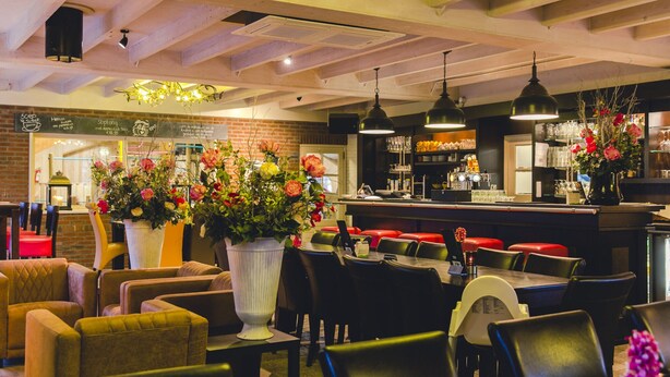 Un interno ristorante con travi in legno, lampade pendenti e un'area bar.