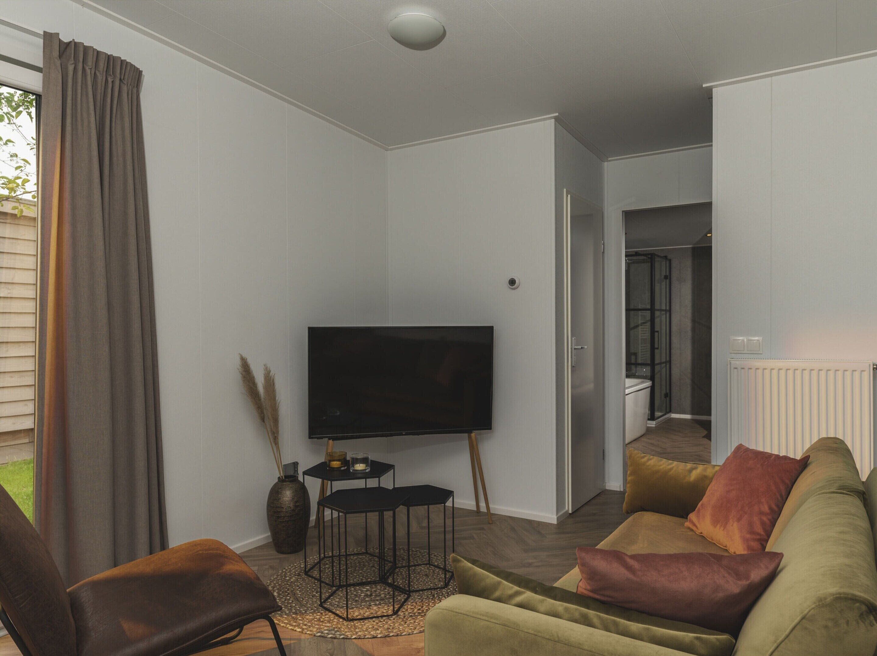 Una sala de estar moderna con un televisor de pantalla plana, un sofá, una mesa de centro y un amplio ventanal con cortinas.
